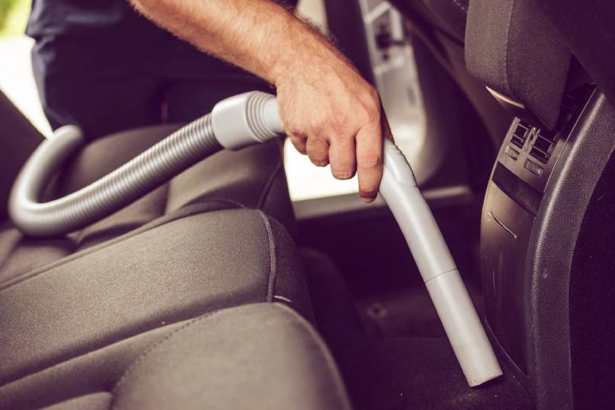 A person using an attachment to clean the seat of a car.